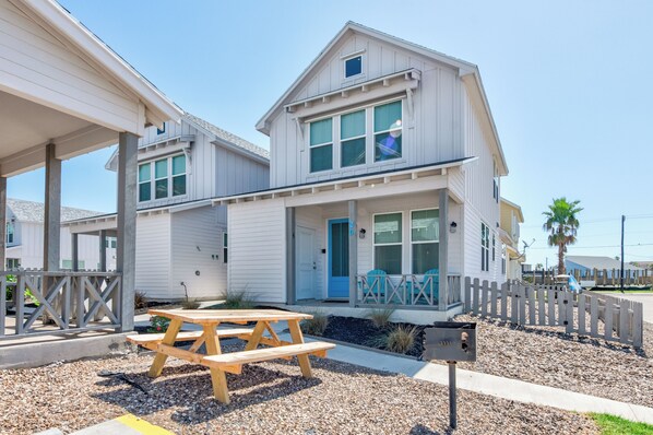 A two-story house with a front porch, a wooden picnic table, and a mailbox. - The best vacation memories are made at the beach! Golf cart available for rent, (Port Aransas)