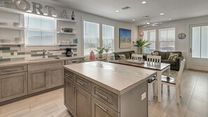 A modern kitchen with a central island, built-in cabinets, and a dining area with a white table and chairs. - The best vacation memories are made at the beach! Golf cart available for rent, (Port Aransas)