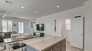 A modern kitchen with a central island, built-in cabinetry, and a dining area with a white table and chairs. - The best vacation memories are made at the beach! Golf cart available for rent, (Port Aransas)