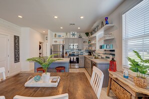 Uma cozinha moderna com uma ilha central, eletrodomésticos de aço inoxidável e uma área de jantar com mesa e cadeiras de madeira.