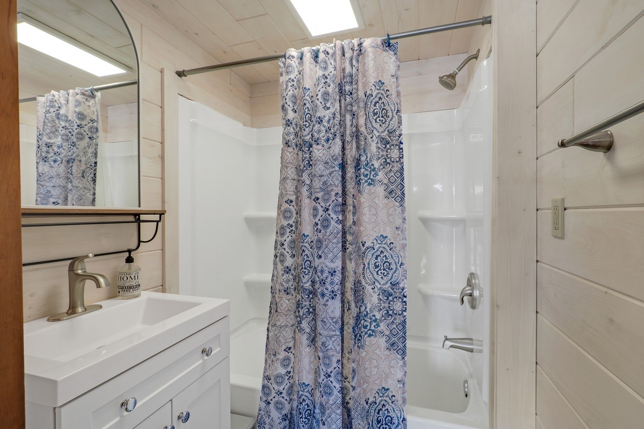 A bathroom with a white sink, a mirror, a shower with a patterned curtain, and a bathtub.