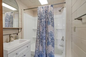 A bathroom with a white sink, a mirror, a shower with a patterned curtain, and a bathtub. - The Banks - Rustic and Waterfront, Secluded and Special, by RedAwning (Onaway)