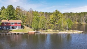 Una casa a la orilla del lago con un muelle y una pequeña embarcación amarrada.