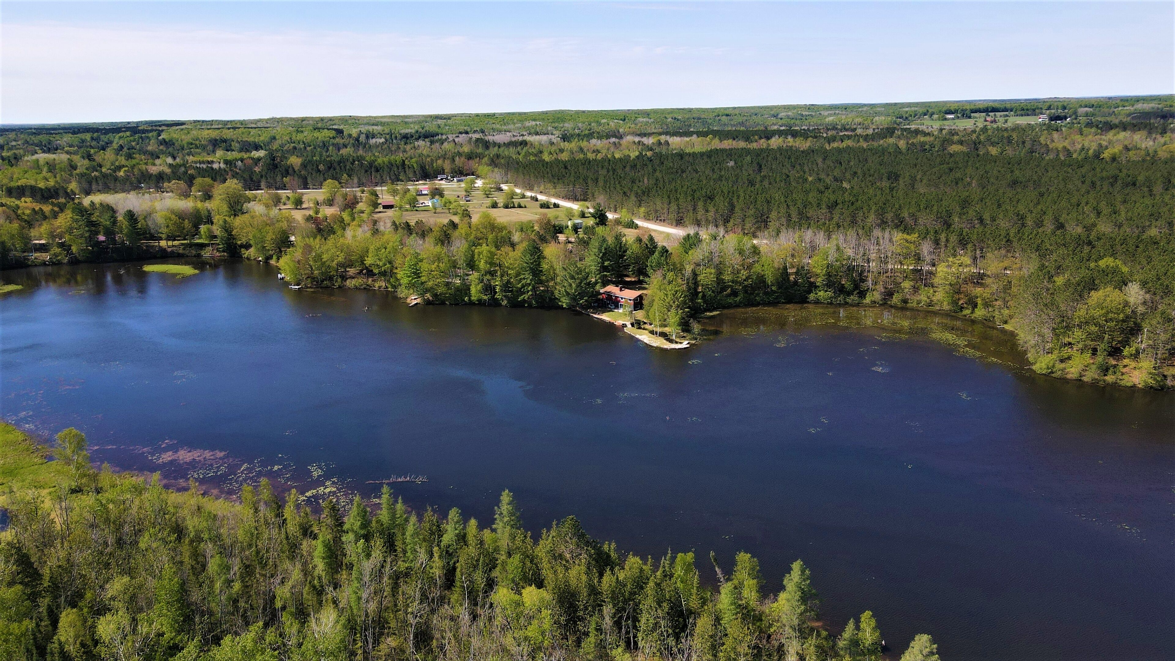 En fastighet vid en sjö med ett hus omgivet av tät skog, en brygga och en fri utsikt över sjön.