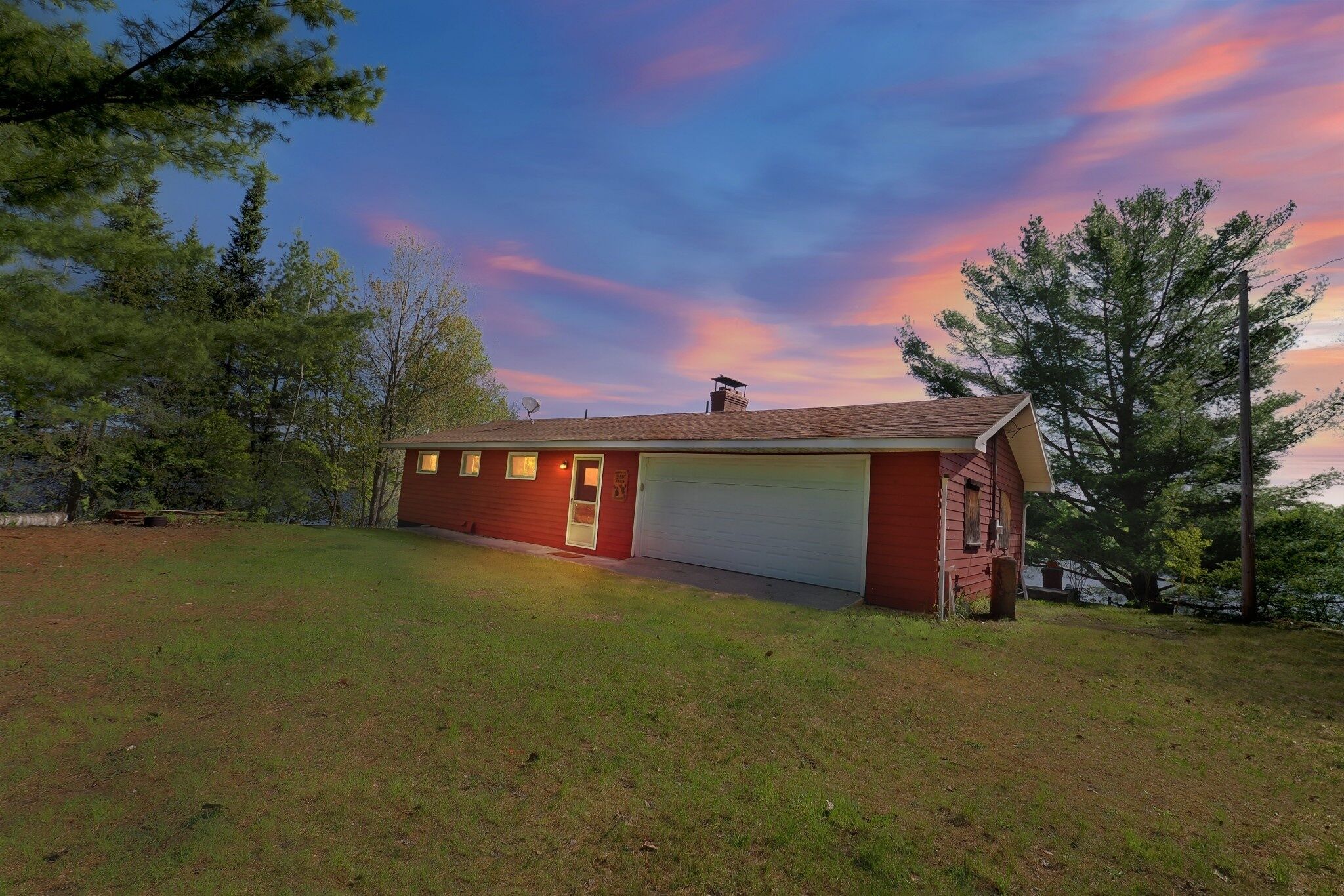 A single-story house with a garage, surrounded by a grassy yard and trees.