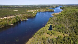An aerial view of a river winding through a densely forested area with a small island and a few buildings along the shore. - The Banks - Rustic and Waterfront, Secluded and Special, by RedAwning (Onaway)