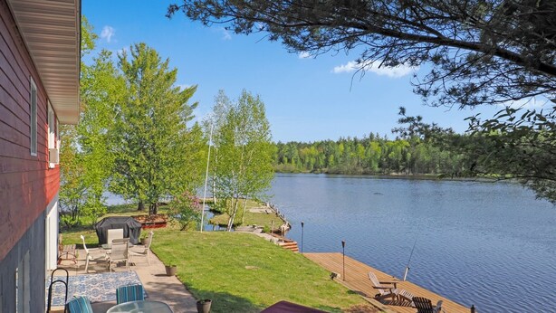 Un patio junto al lago con mobiliario exterior, una parrilla cubierta y un muelle que se adentra en el agua.