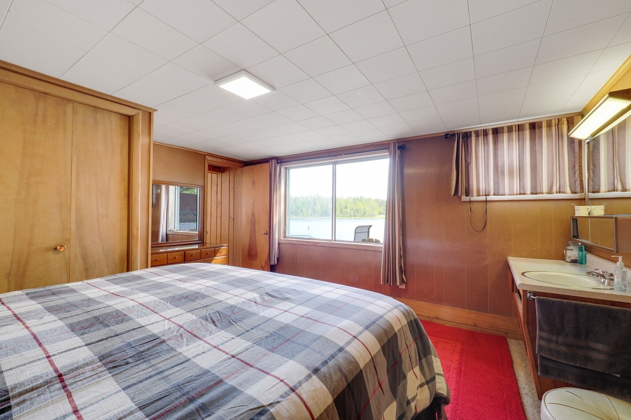 A hotel room with a large bed, a wooden wardrobe, a bathroom with a mirror and sink, and a window with a view of the outdoors.