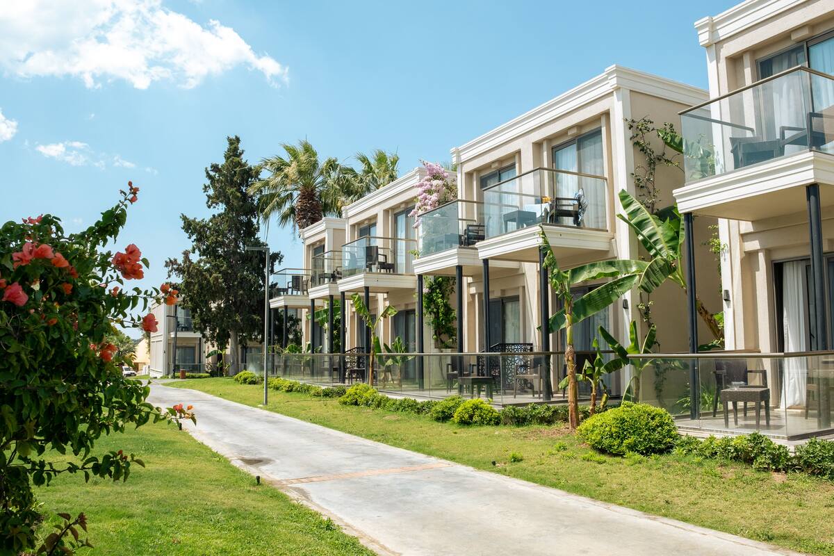 A row of modern, two-story buildings with balconies, surrounded by lush greenery and palm trees.