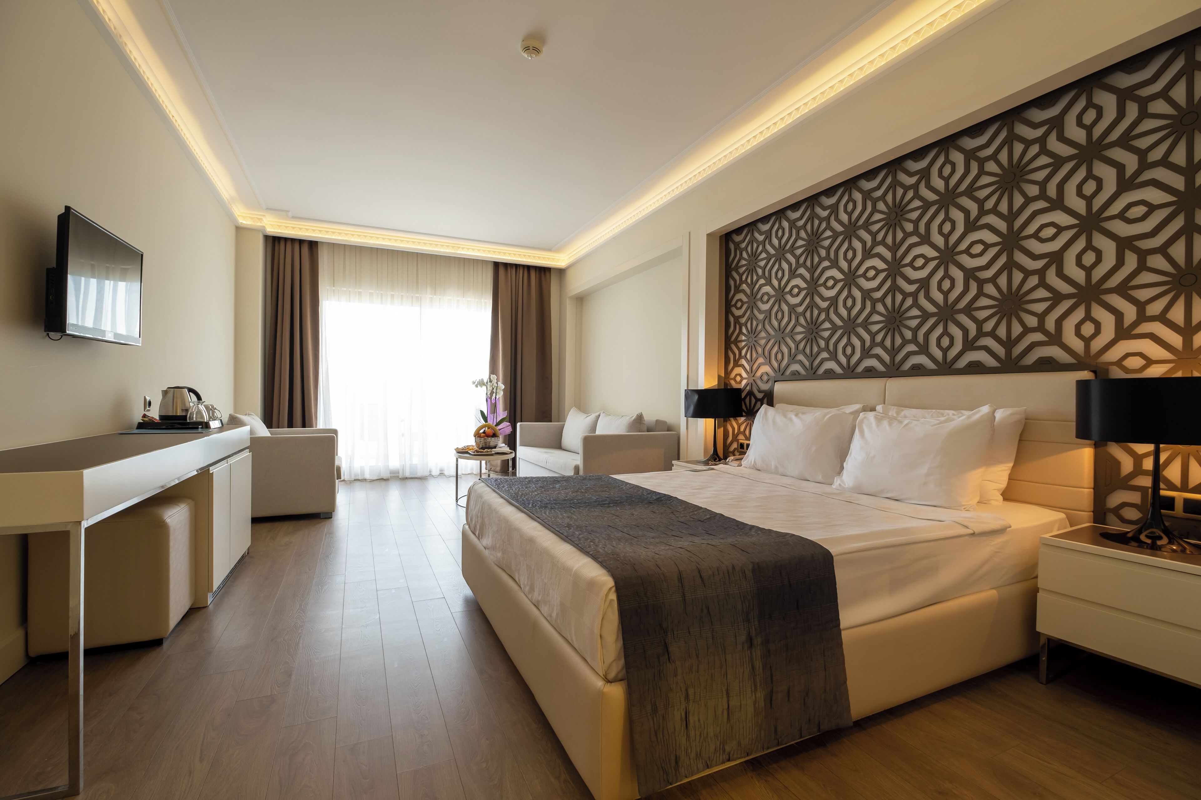 A modern hotel room with a large bed, a desk, a flat-screen TV, and a decorative wall panel.