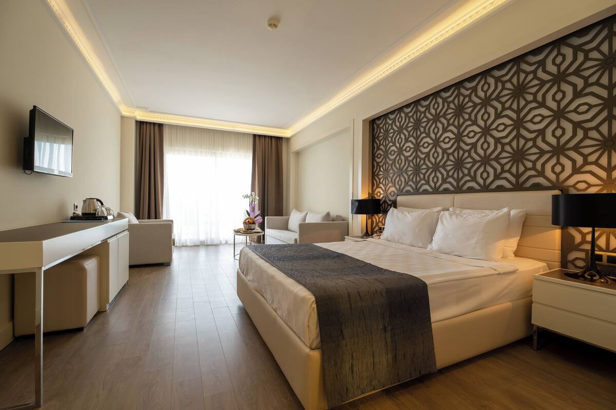 A modern hotel room with a large bed, a desk, a flat-screen TV, and a decorative wall panel.