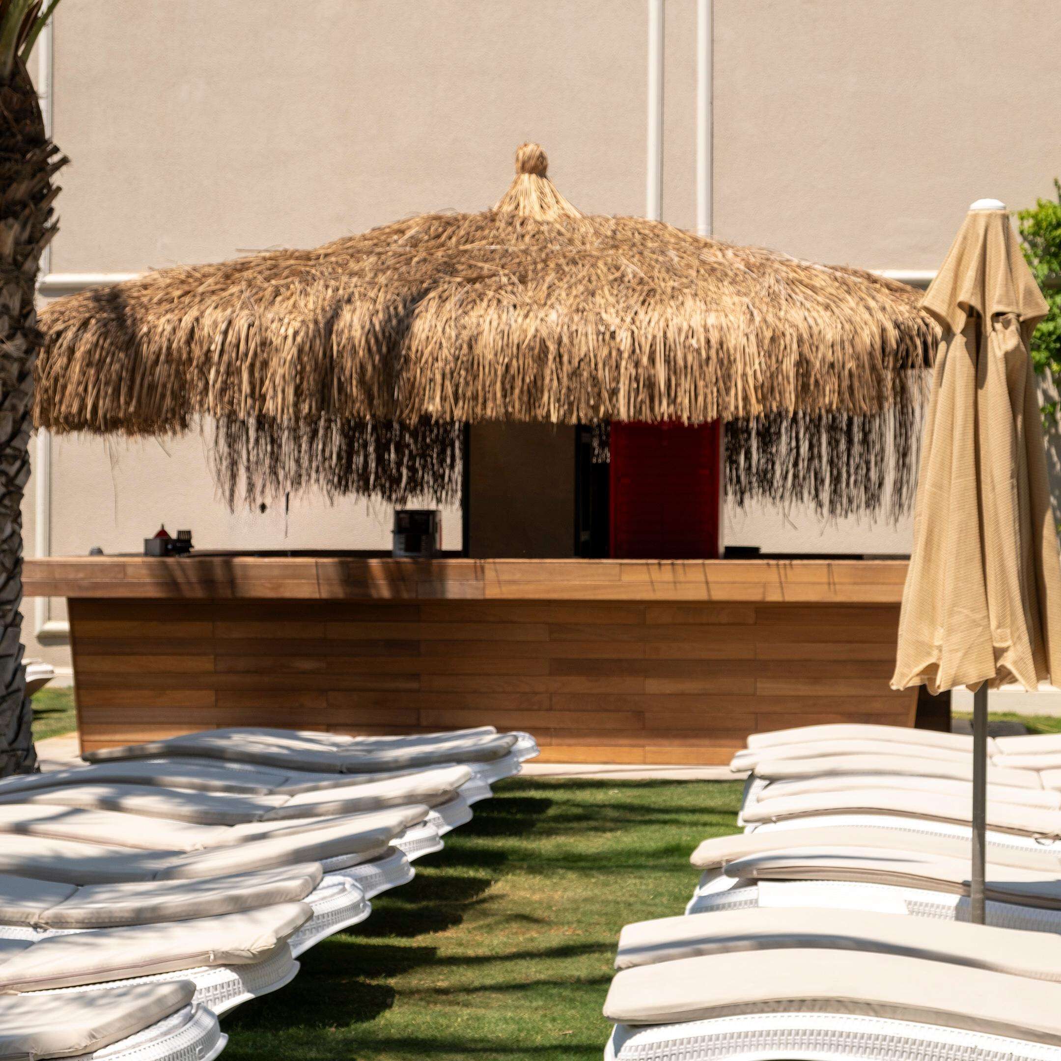 A thatched-roof outdoor bar area with lounge chairs and a wooden counter.