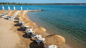 Une plage bordée de rangées de chaises longues blanches et de parasols en chaume.