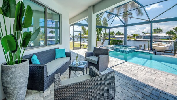 Uma área de estar ao ar livre moderna, com piscina, mobiliário de vime e grandes janelas com vista para os arredores.