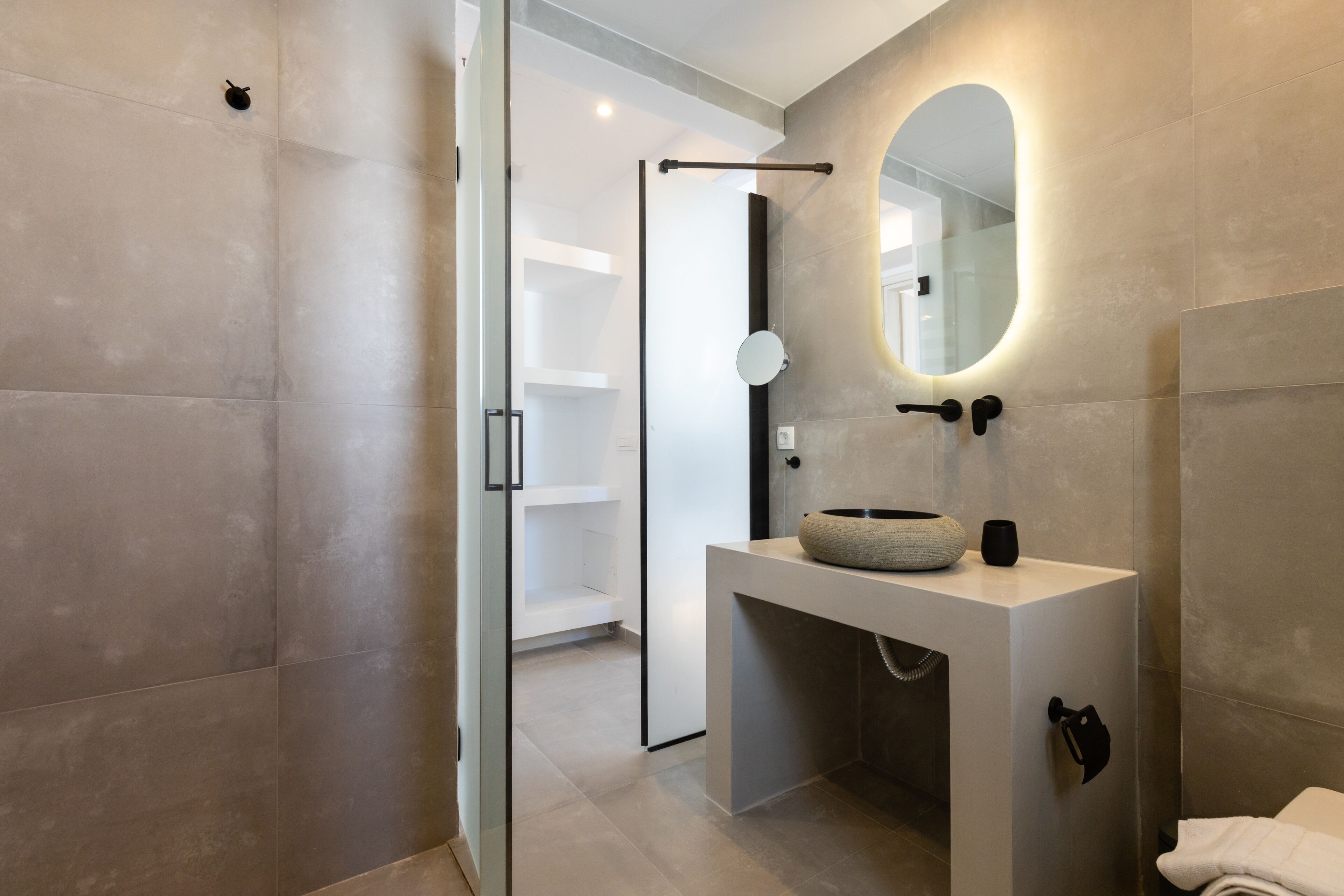 Une salle de bain moderne avec une douche à parois de verre, un miroir rond et un lavabo blanc doté d’une cuve en pierre.