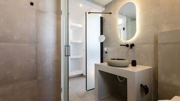 Une salle de bain moderne avec une douche à parois de verre, un miroir rond et un lavabo blanc doté d’une cuve en pierre.