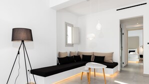 A modern living room with a black sofa, a white coffee table, and a floor lamp. - SERAPIAS SUITES (Santorini)