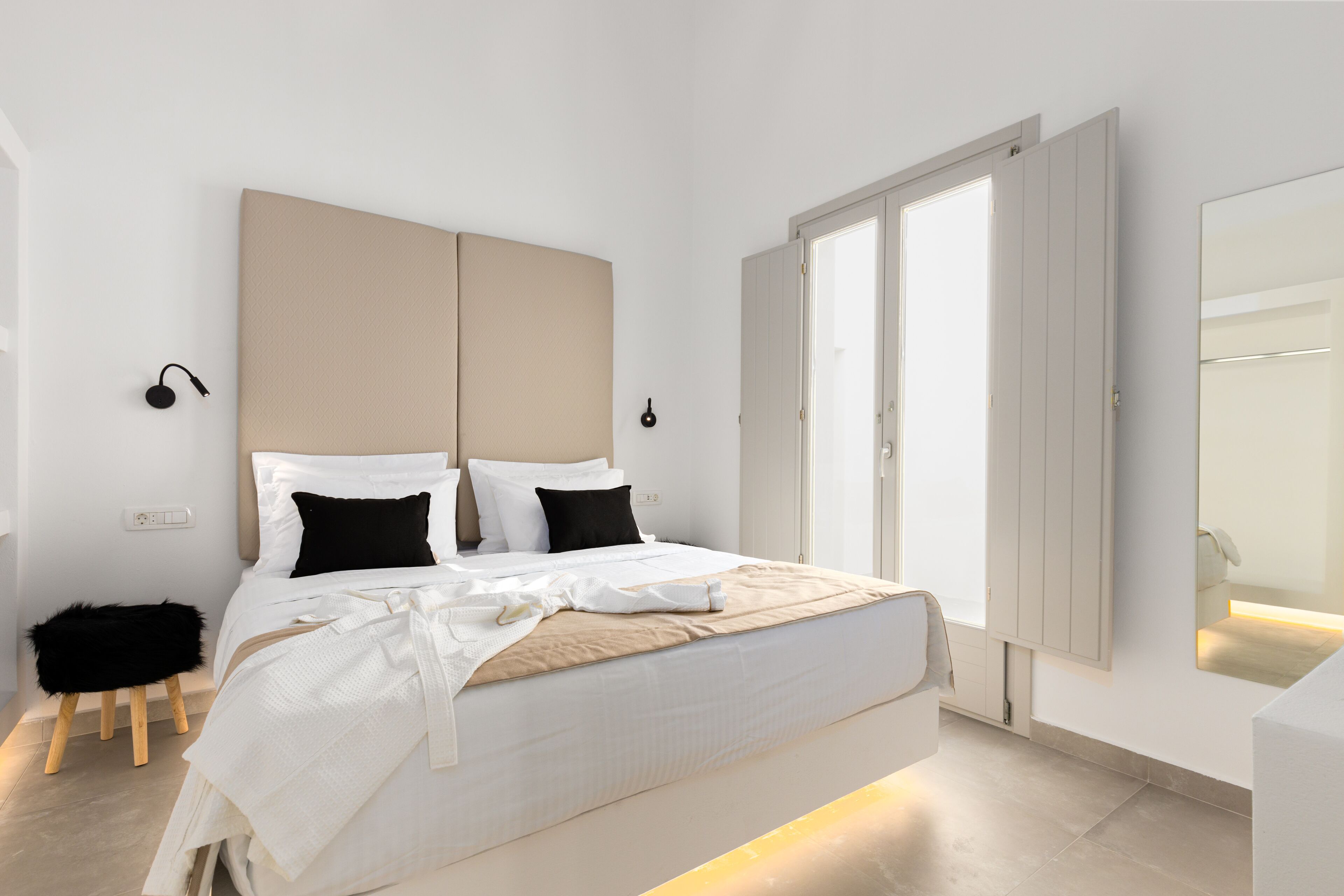 A modern bedroom with a large bed, two bedside tables, a small stool, and a large mirror.