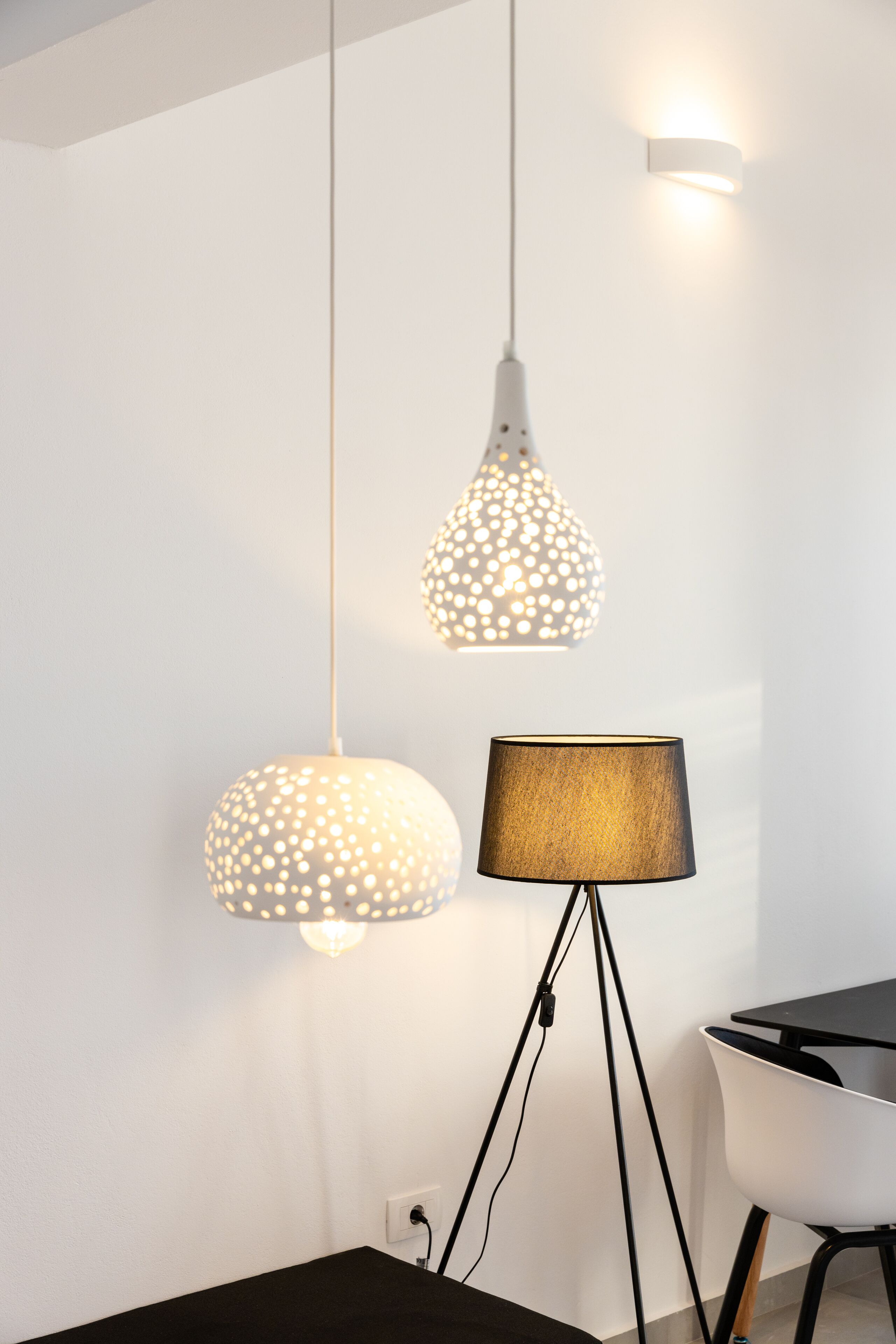 Una habitación moderna con una mesa negra y una silla blanca. Hay dos lámparas colgantes con un diseño original en el techo.