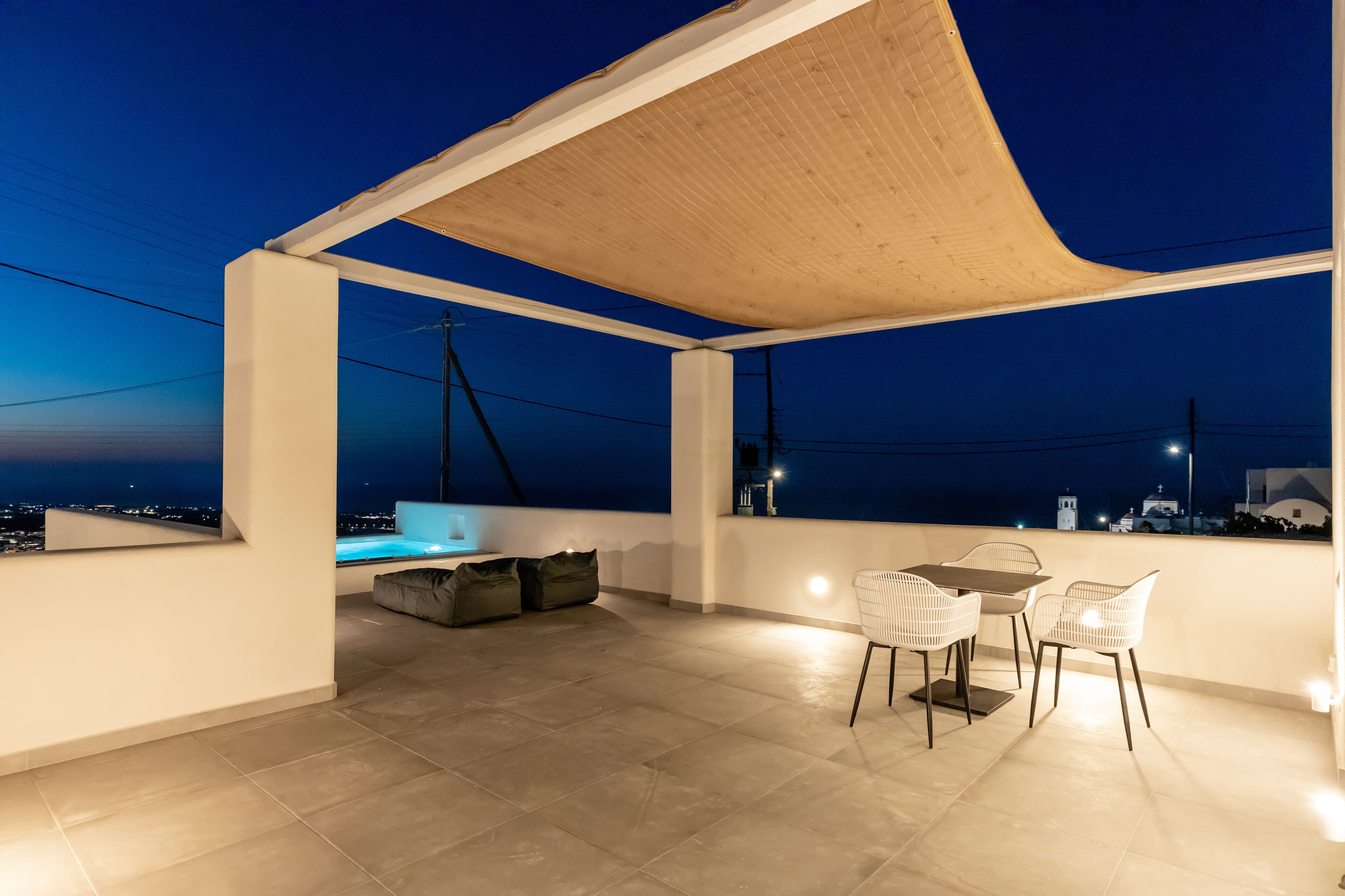A rooftop terrace with a table and chairs, a sofa, and a view of the cityscape at night.