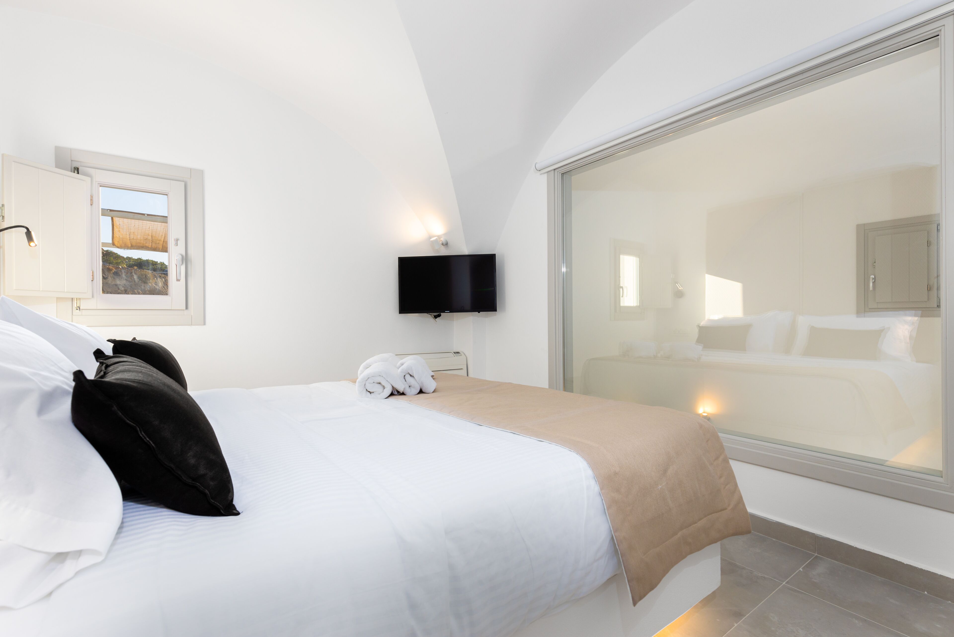 A hotel room with a bed, a television, a window with a view, and a sliding door.
