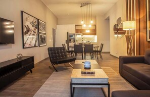 A modern living room with a sofa, a coffee table, and a TV. There is a dining area with a table and chairs. The kitchen is visible in the background. - w* | Amazing 2BR in Miraflores (Miraflores)