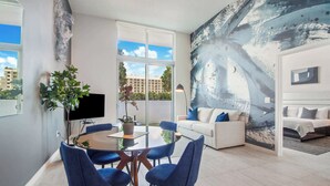 A modern living room with a dining area, a large abstract painting, and a view of buildings through the windows. - One Bedroom Condo King Bed With City Views (Miami)