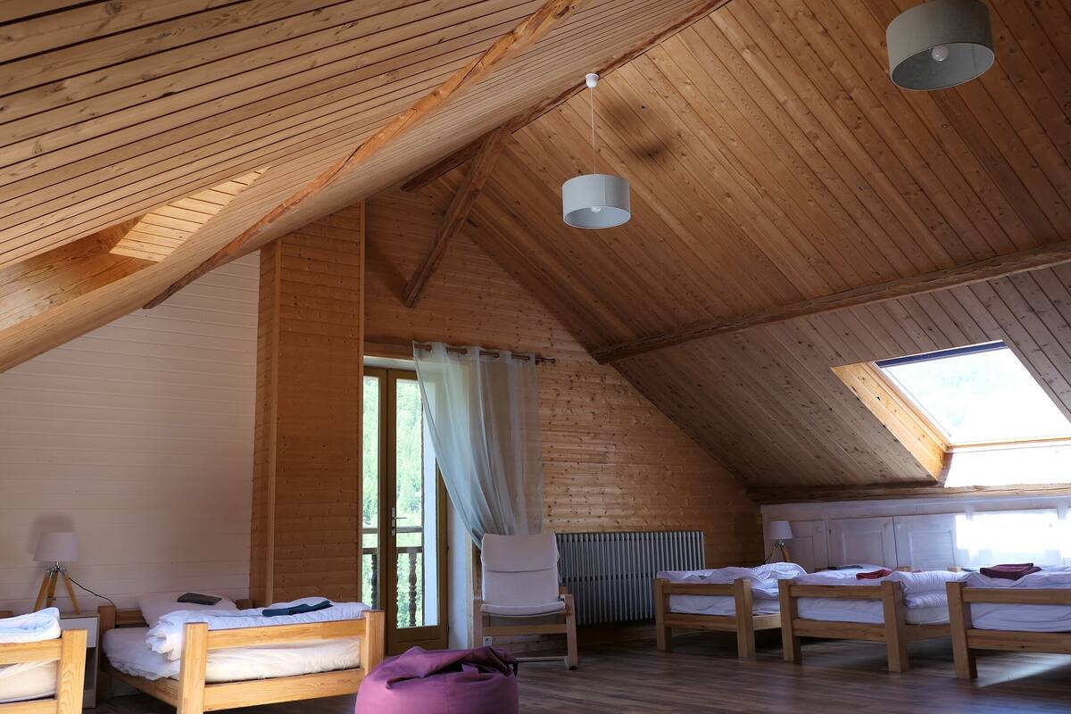 Acogedor dormitorio en ático con vigas de madera, tragaluces y cuatro camas de madera.