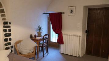 Een gezellige kamer met een bed, een klein tafeltje met een plant, een stoel en een deur.