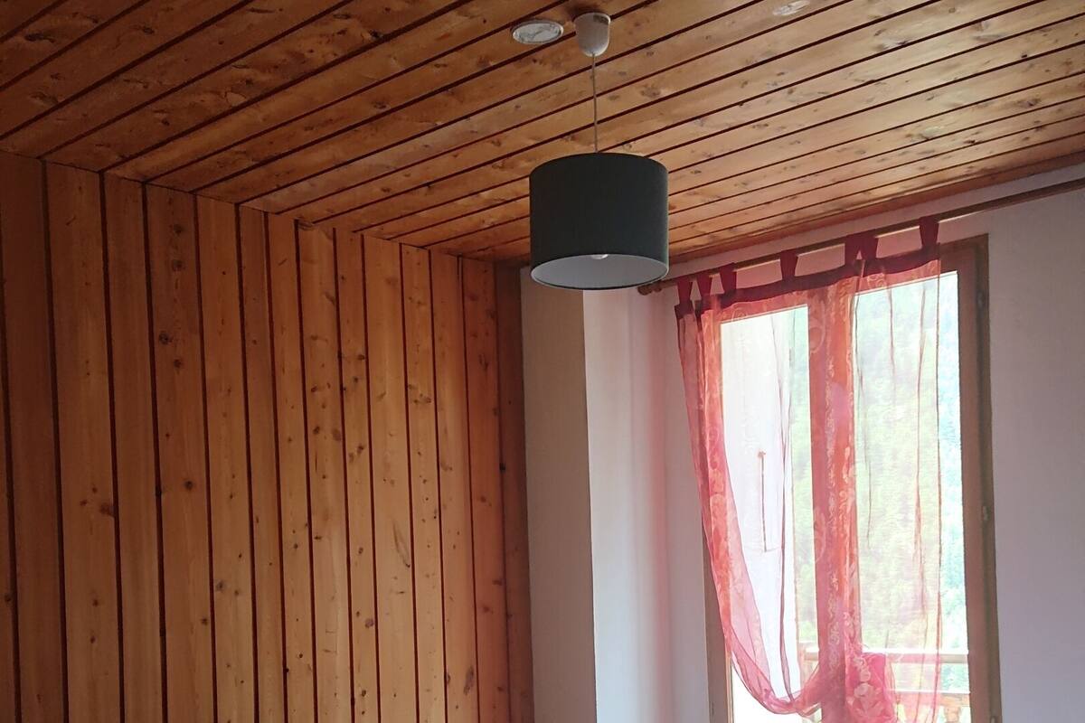 Una habitación con paredes de paneles de madera, una cama con ropa de cama blanca y toallas color turquesa, una ventana con cortinas rojas y una lámpara colgante.