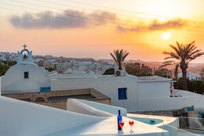 A white building with a dome and a cross on top, overlooking a cityscape at sunset. - Sunborn Oia Suites (Santorini)