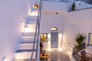 A white-walled building with a staircase leading to an upper level. There is a door with a window, a small table with a plant, and a railing on the staircase. - Sunborn Oia Suites (Santorini)