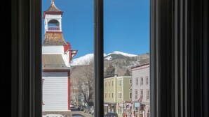 A view through a window of a town with a church steeple and snow-capped mountains in the background. - Fillmore Loft at Public House on Elk Ave (Crested Butte)