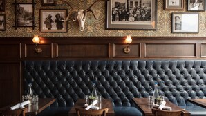 A restaurant with a dark blue upholstered bench seating area, framed photographs on the wall, and a large antler mounted above the seating. - Fillmore Loft at Public House on Elk Ave (Crested Butte)