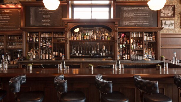 A bar with a wooden interior, multiple liquor bottles, and bar stools. - Fillmore Loft at Public House on Elk Ave (Crested Butte)