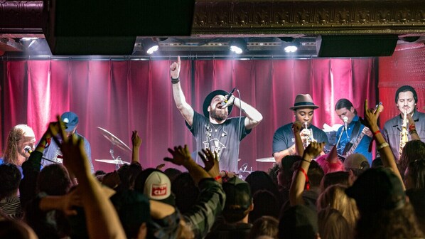 A band performing on stage with a crowd in the foreground.