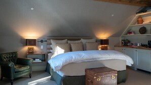 Un dormitorio acogedor con una cama grande, dos lámparas de noche, un sillón verde, una mesita con libros y una maleta.