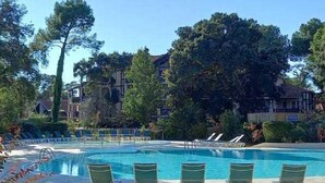 Une piscine entourée d’arbres et de bâtiments, avec des chaises longues à proximité.