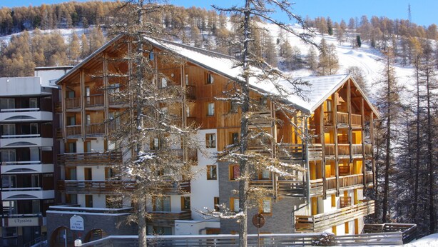 A multi-story wooden lodge with balconies, surrounded by snow-covered trees and a ski slope in the background. - L' IDEAL at Ecrin des Neiges. (Vars)
