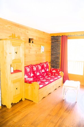 A wooden cabin with a red sofa, a wooden cabinet, and a small white stool. - L' IDEAL at Ecrin des Neiges. (Vars)