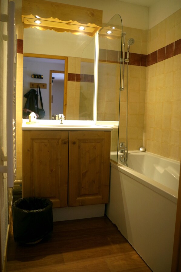 A small bathroom with wooden cabinets, a white sink, and a bathtub.