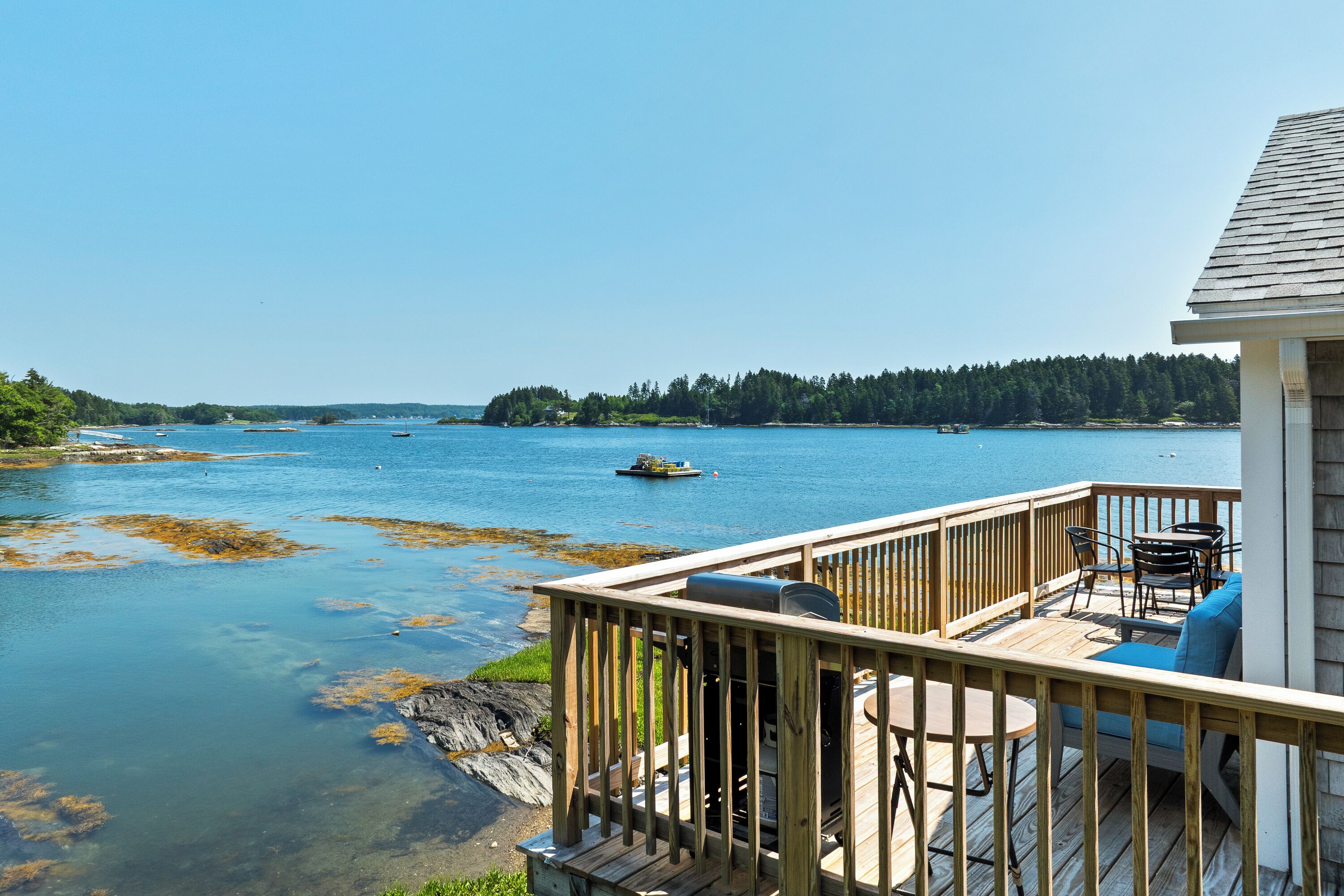 A wooden deck with outdoor furniture overlooking a calm body of water, with a forested island in the distance.