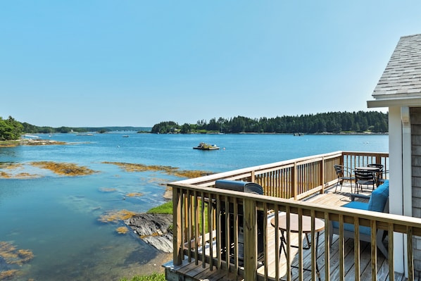 A wooden deck with outdoor furniture overlooking a calm body of water, with a forested island in the distance.