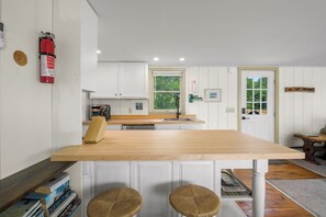 A kitchen with white cabinets, a wooden countertop, and a fire extinguisher mounted on the wall.