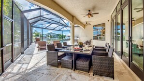 Un patio techado al aire libre con mobiliario de mimbre, una mesa de comedor y un ventilador de techo.