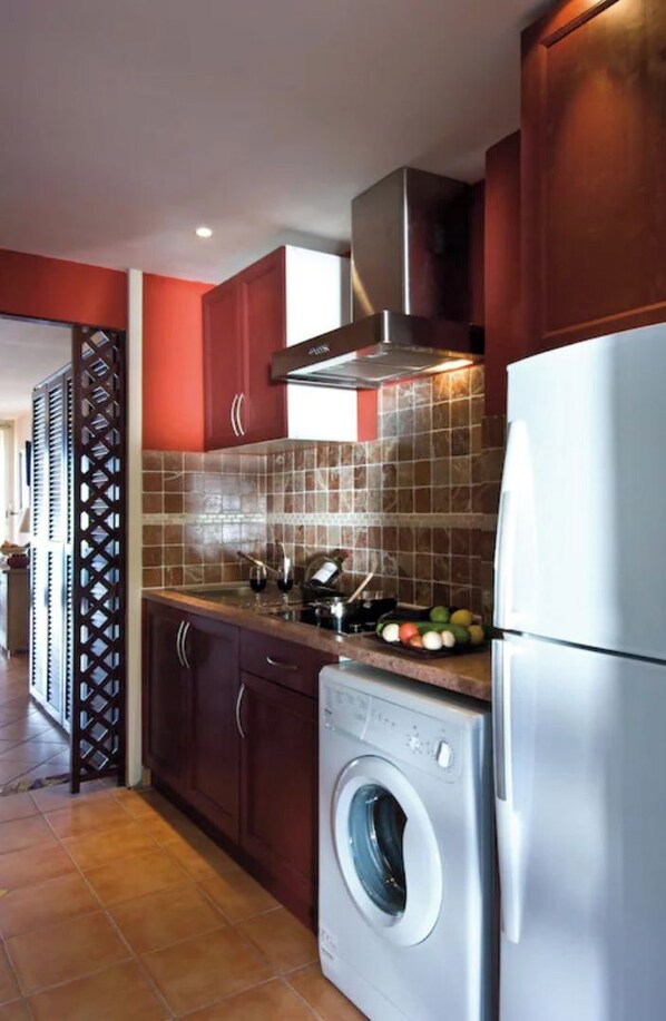 A compact kitchen with a built-in washer and dryer, a stainless steel refrigerator, and a tiled backsplash.