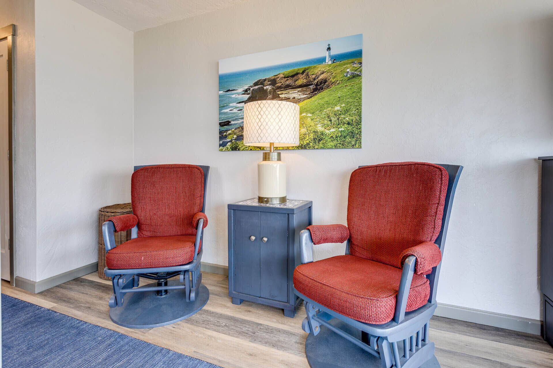 A room with two rocking chairs, a small cabinet, and a painting of a lighthouse.