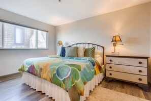 A bedroom with a bed, bedside lamps, a nightstand, and a window.