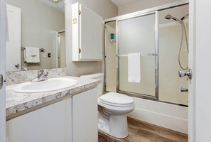 A bathroom with a white sink, a toilet, and a glass-enclosed shower. - Ocean Front Condo, View of Lighthouse, Walk to Everything, Nye Beach! (Newport)