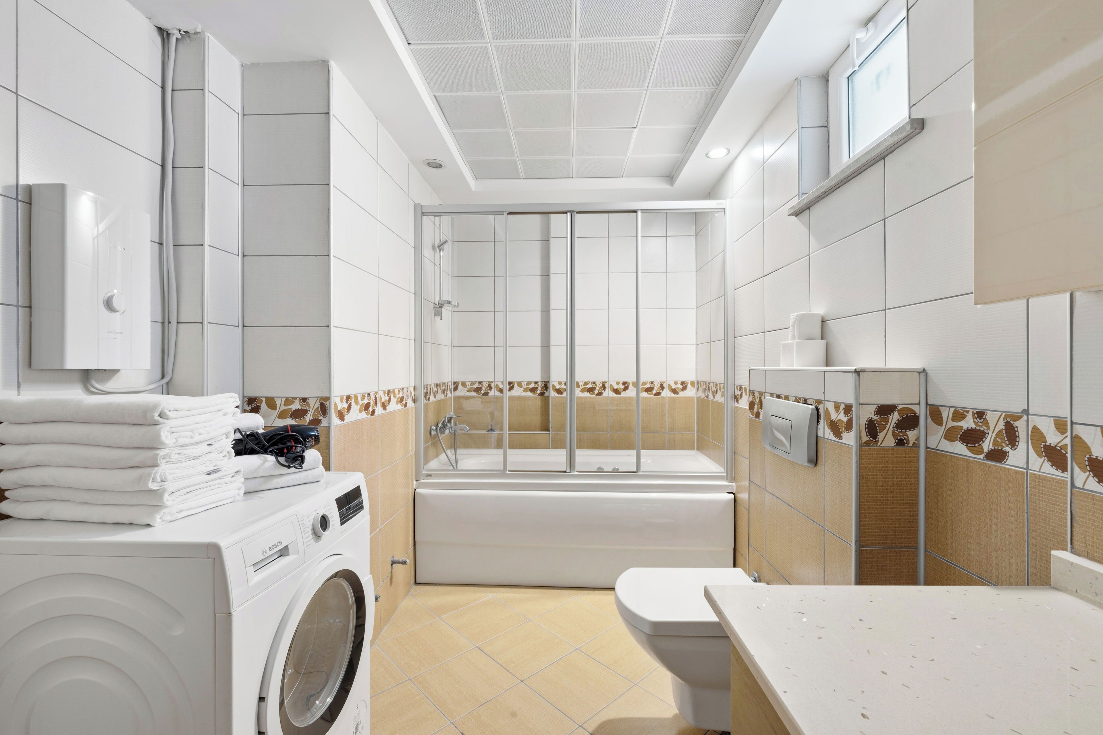 A modern bathroom with a washing machine, a bathtub, and a toilet.